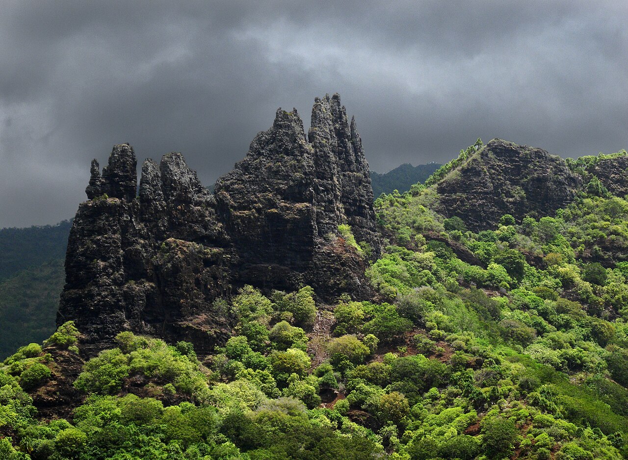 Aiguilles rocheuses sombres couvertes de végétation verte sous un ciel d'orage, vallée de Nuku Hiva
