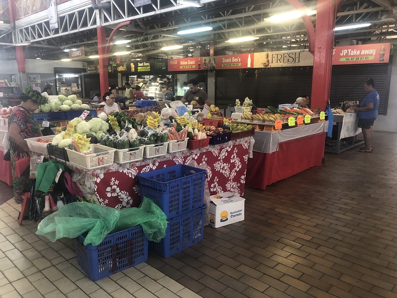 Étals de fruits et légumes au marché de Papeete, avec les snacks du fond de la halle