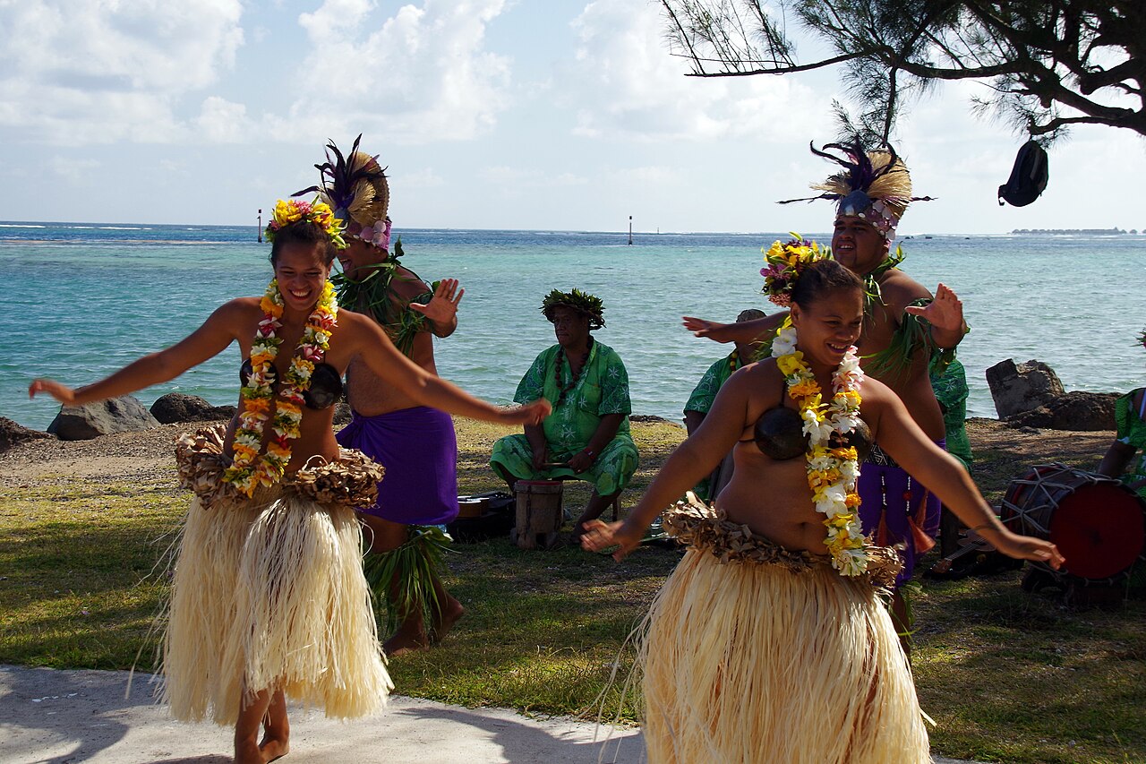 Danseurs en tenues de fibres et couronnes de fleurs sur une pelouse au bord du lagon à Moorea