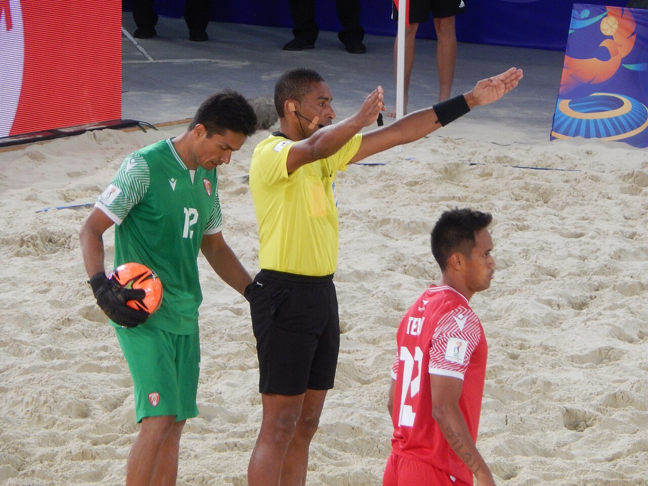 Le gardien tahitien en vert tenant le ballon à côté de l'arbitre, avec un joueur en rouge au premier plan