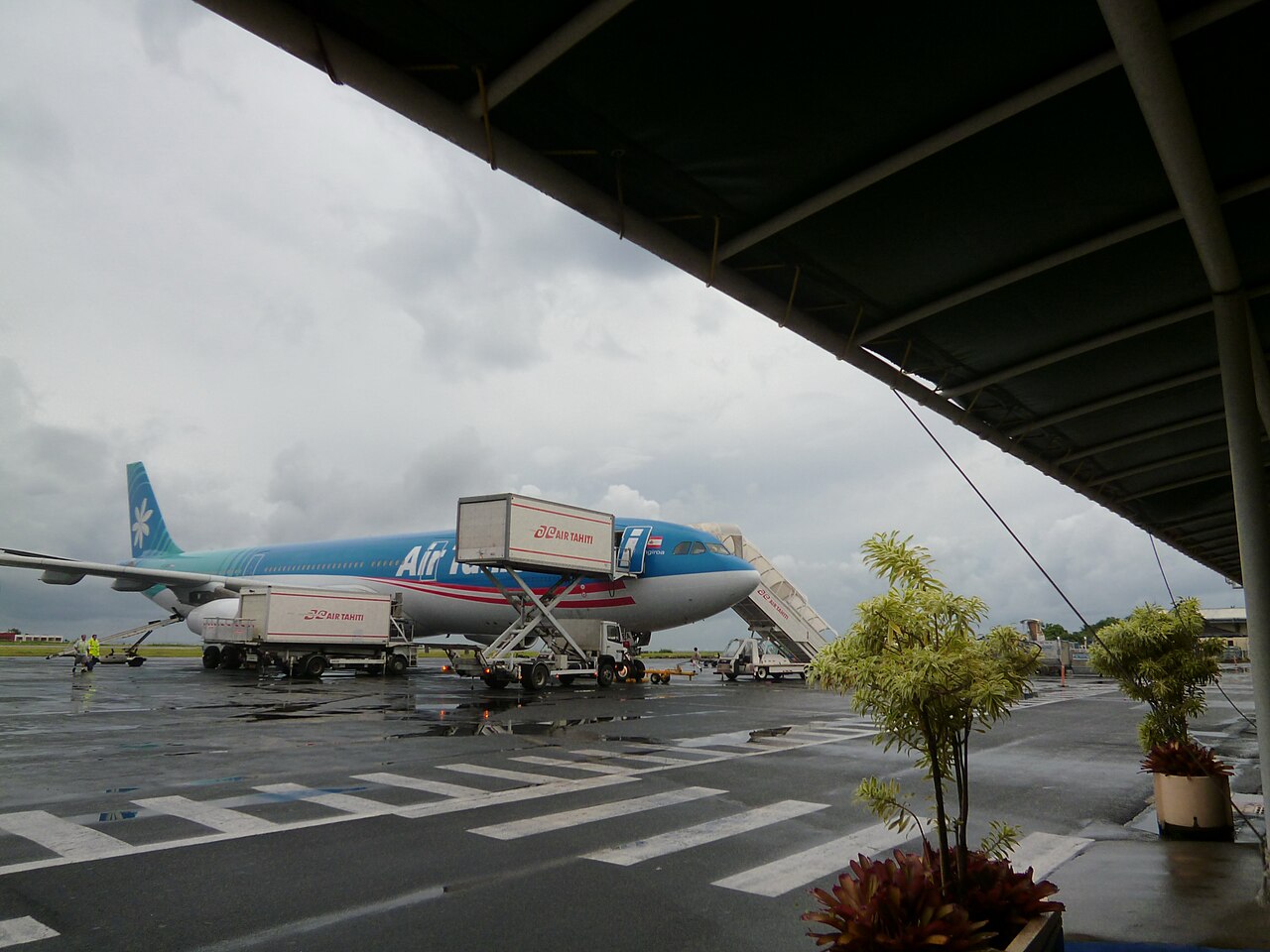 Airbus d'Air Tahiti Nui et chariots de service sur le tarmac de Tahiti-Faa'a sous un ciel couvert