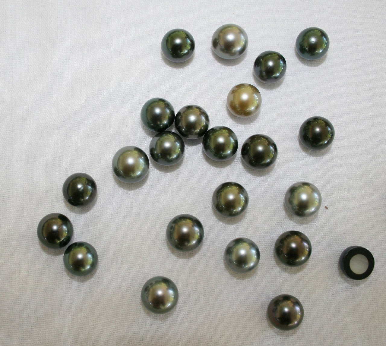 Perles de Tahiti noires, vertes, grises et dorée posées sur un tissu blanc